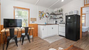 A compact kitchen with white cabinets, a black refrigerator, a wooden dining table with two chairs, and a television. - Summer Escape with Swim Hole and Golf Cart Rental (Spring Branch)