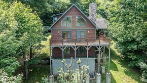 Eine zweistöckige Holzhütte mit einem Balkon, umgeben von dichtem Wald.