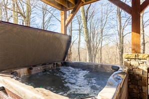 Un bain à remous doté d’un mur en pierre et de poutres en bois, entouré d’arbres.