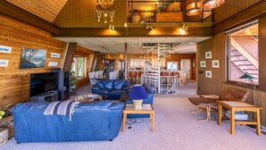 Ein geräumiger Wohnbereich mit hoher Decke, Holzwänden, einer Treppe und einer Küchenzeile.
