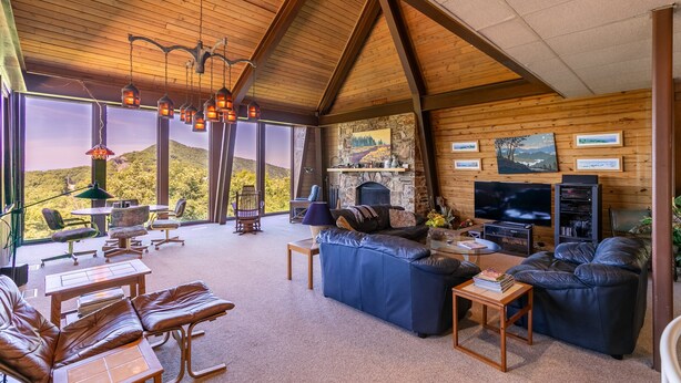 Ein geräumiges Wohnzimmer mit Ledersofas, einem Steinkamin, einem großen Fernseher und einem Essbereich mit Tisch und Stühlen.