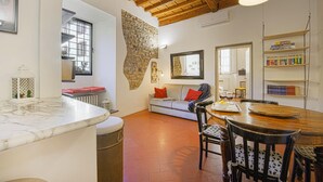 A cozy living area with a stone wall, a wooden ceiling, a dining table with chairs, and a bookshelf. - Bombarde - Flo Apartments (Firenze)