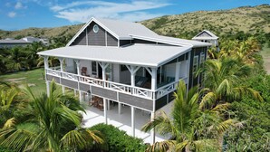 A two-story house with a balcony and a covered porch, surrounded by lush greenery and hills in the background. - Spacious 2 BR cottage with gorgeous views  (Basseterre)