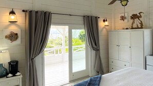 A bedroom with a bed, a ceiling fan, a window with curtains, a desk with a lamp, and a view of the outdoors. - Spacious 2 BR cottage with gorgeous views  (Basseterre)