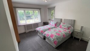 Une chambre avec deux lits, une table de chevet, une fenêtre et un radiateur.