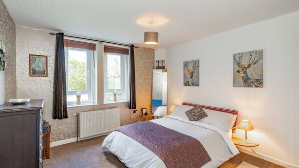 A bedroom with a large bed, a dresser, a window with curtains, a radiator, and artwork on the walls. - Home-from-home; 10 mins from city centre; Free on-street parking; Well-equipped (Edinburgh)