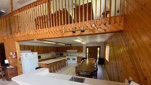 A spacious kitchen with a long island counter, wooden paneling, and a view of the adjacent dining area.