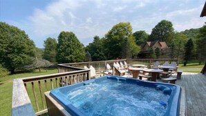 A hot tub on a wooden deck with outdoor furniture and a view of a house and trees.