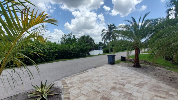 A paved pathway with palm trees and greenery, leading to a body of water. - Beautiful, cozy, clean & fresh house on a canal with private ramp, spce to moore (Bokeelia)