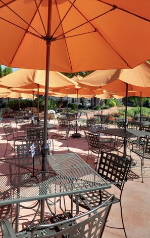 Espace extérieur aménagé avec des parasols orange et des tables et chaises en métal.