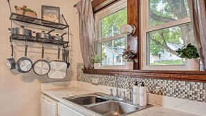 Una cocina con un lavaplatos doble, un escurreplatos y una ventana que da a una casa y árboles.