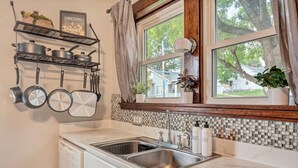A kitchen with a double sink, a dish rack, and a window with a view of a house and trees.