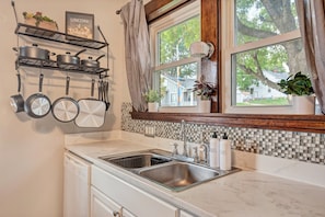 A kitchen with a double sink, a dish rack, and a window with a view of a house and trees.