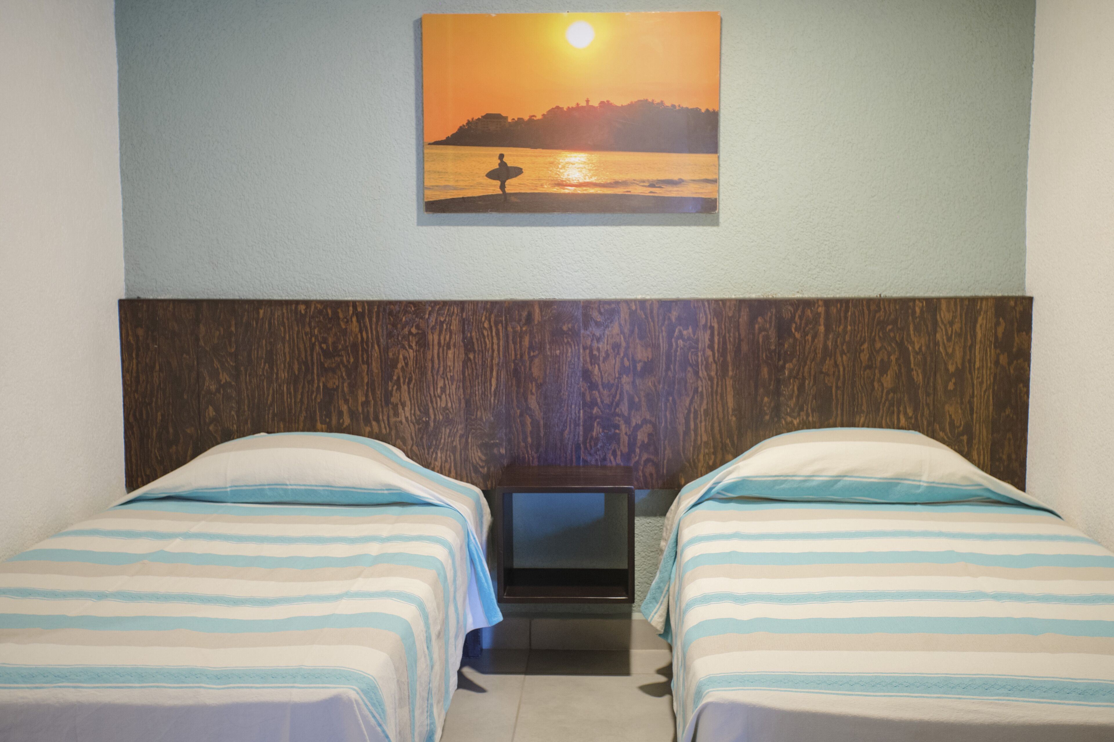 A hotel room with two beds, a wooden headboard, and a painting of a sunset over water on the wall.