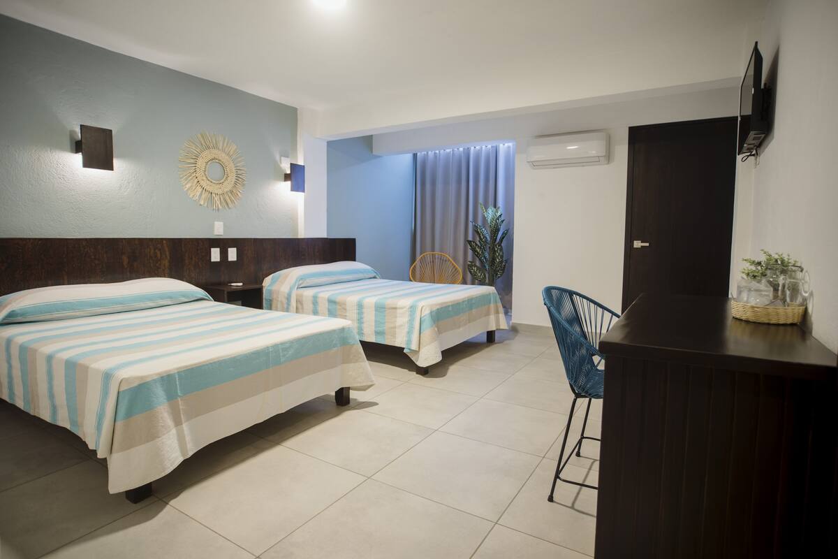 Une chambre d’hôtel avec deux lits, un bureau, une chaise, une télévision et une fenêtre avec des rideaux.