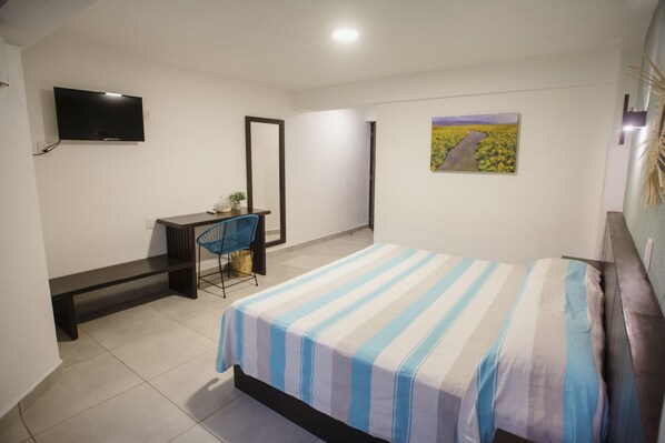A bedroom with a bed, a desk, a chair, a TV, and a painting on the wall.