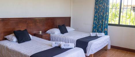 Een hotelkamer met twee bedden, elk met een witte dekbedovertrek en zwarte kussens. Op de bedden liggen handdoeken met de tekst 'CAMINO DEL SOL'.
