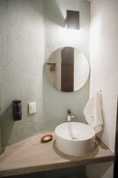 Un baño con un espejo redondo, un lavabo blanco, una toalla y un dispensador de jabón.