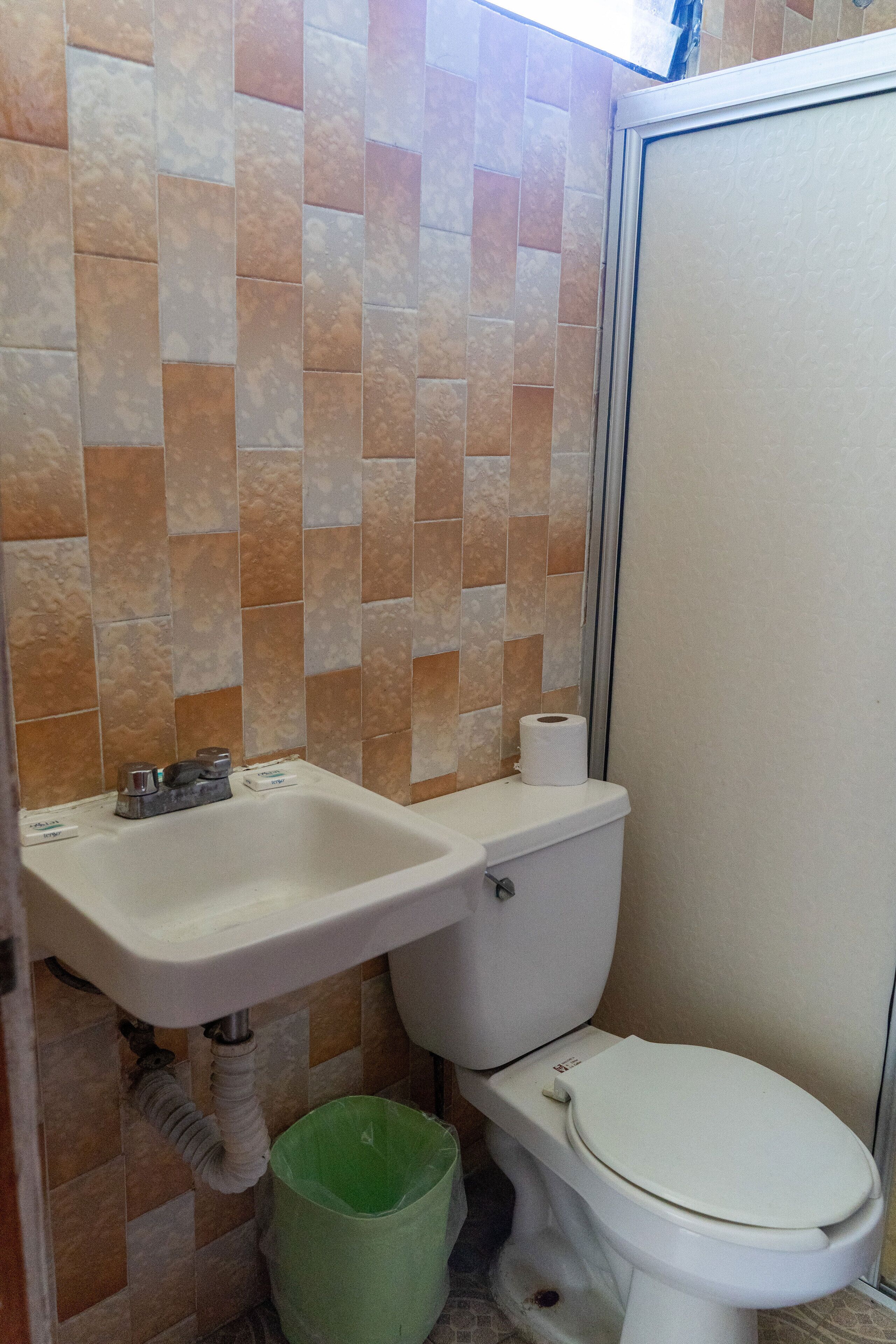 Een badkamer met toilet, wastafel en groene prullenbak.