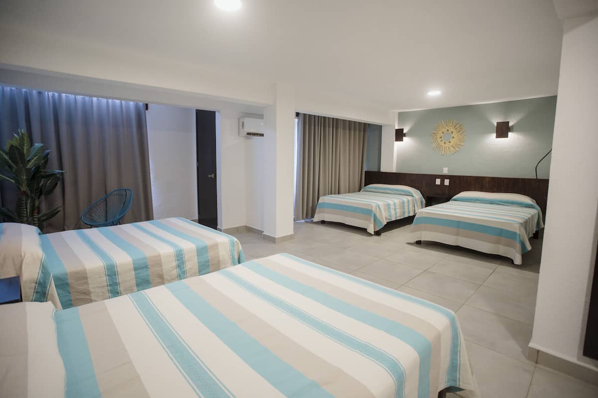 Une chambre d’hôtel avec deux lits simples, une chaise, une plante en pot et un climatiseur fixé au mur.