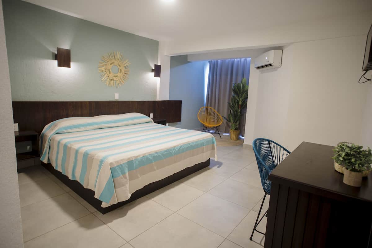 Une chambre à coucher comprenant un lit, un bureau, une chaise, une plante en pot et un climatiseur fixé au mur.