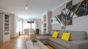 A modern living room with a grey sofa, yellow cushions, a wooden coffee table, and abstract art on the wall.