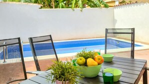 A poolside table with chairs, a bowl of fruit, a potted plant, and a glass of green drink.