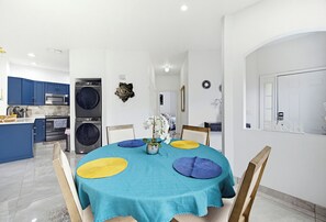 Een moderne keuken met inbouwapparatuur, een eethoek met een blauwgroene tafelkleed, en een witte deur met een beveiligingsmechanisme.