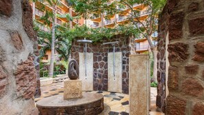 A stone-walled courtyard with a circular stone platform, a stone sculpture, and a metal shower enclosure. - Disney Aulani Deluxe Oceanview Studio Villa! (Kapolei)