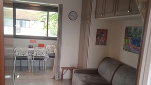 Une pièce avec un canapé gris, une table à manger avec des chaises, une horloge au mur et un tableau.
