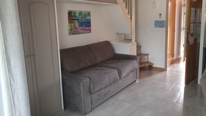 Une pièce avec un canapé gris, un tableau, un escalier et une porte avec une pancarte.