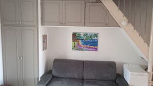 Une pièce avec un canapé gris, un tableau représentant une scène de plage et un escalier.