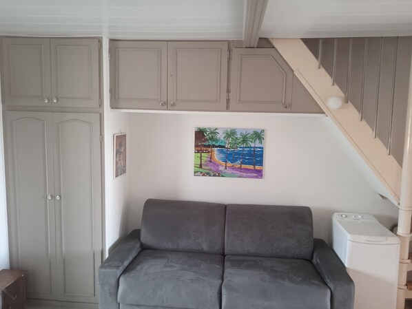 A room with a grey sofa, a painting of a beach scene, and a staircase. - APARTMENT IN SAINT CYPRIEN, OFF-SEASON: 250 € PER WEEK (Saint-Cyprien)