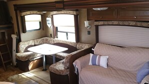 Un intérieur de camping-car compact comprenant un coin cuisine, un espace repas, un coin salon avec un canapé et une table, ainsi qu’une fenêtre laissant entrer la lumière naturelle.