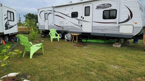 Un véhicule récréatif est stationné dans une zone herbeuse, avec une chaise verte et une petite table à proximité.