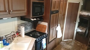 Une cuisine de taille réduite, dotée de meubles de rangement en bois, d’une cuisinière, d’un four à micro-ondes et d’un évier.