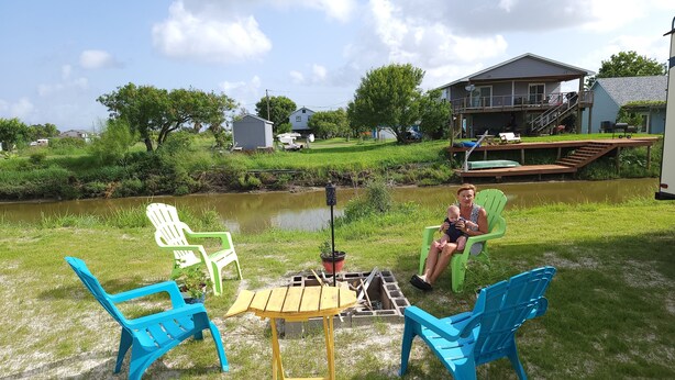 Une terrasse avec des sièges d’extérieur et une petite table, d’où l’on peut admirer un plan d’eau et une maison au loin.