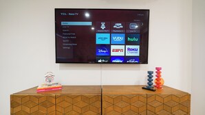 A TCL Roku TV mounted on a wall displaying various streaming services.