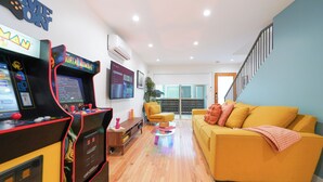 A living room with a yellow sofa, a gaming console, and a staircase.