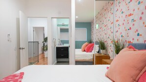 A bedroom with a bed, a nightstand, a dresser, and a door leading to another room.