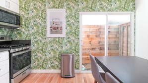 A kitchen with a modern stove, a trash can, and a framed picture on the wall.