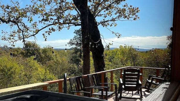 Un jacuzzi con cubierta de madera y sillas, rodeado de árboles y un cielo despejado.