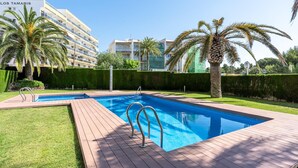A swimming pool with a wooden deck, surrounded by palm trees and a hedge. - Perfect for a vacation of disconnection (Miami Platja)