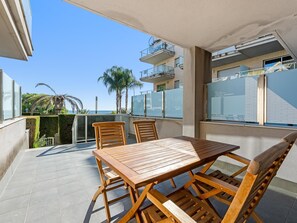 Ein Balkon mit Holztisch und -stühlen, Blick auf das Meer und ein Gebäude mit Balkonen im Hintergrund.