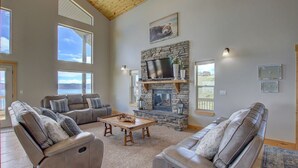 A spacious living room with leather sofas, a stone fireplace, and a large TV.