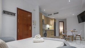 Una habitación de hotel moderna con una cama, un pequeño kitchenette, un comedor y un televisor montado en la pared.