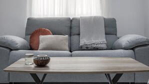 Un sofá gris con dos cojines, una manta de lana gris y una mesa de centro de madera con un bol y dos tarros.
