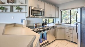 A modern kitchen with a built-in microwave, oven, and dishwasher. There are potted plants on the shelves, and a window providing natural light.