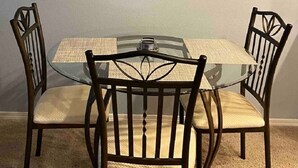 Een eetgedeelte met een glazen tafel en vier stoelen, een decoratief kunstwerk boven de tafel, en een vloerbedekking.