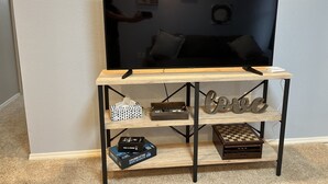 Een televisie op een houten standaard met planken waarop boeken en een schaakbord staan.